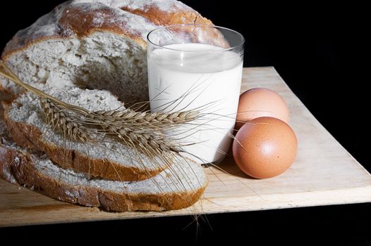 Glass of milk, wheat, eggs and bread over wooden plate