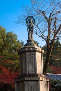 A statue ans red and green trees in a Japanese autumn park 
