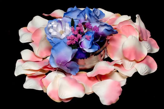 A silver basket with artificial flowers on white and pink rose textile petals on black
