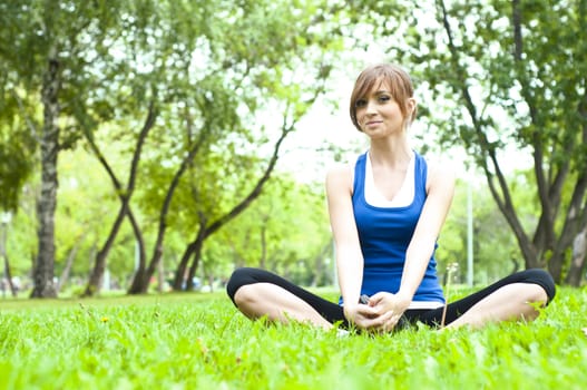 young woman is engaged in yoga, in summer forest on a green grass