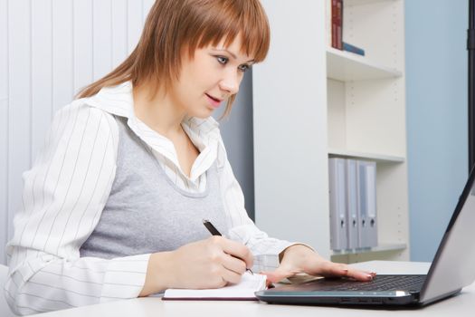 attractive young woman working with laptop on a background of office interior
