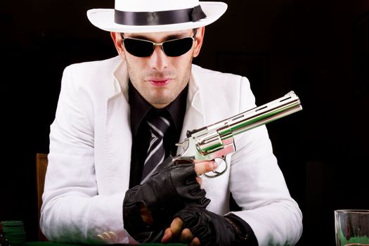 View of a gangster man playing some cards and poker, holding a gun.