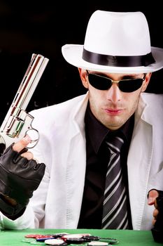 View of a gangster man playing some cards and poker, holding a gun.