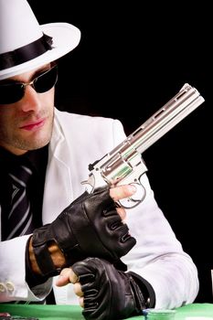 View of a gangster man playing some cards and poker,  holding a gun.