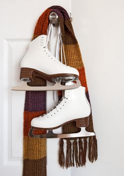Elegant white figure skates and colourful scarf hanging on a door knob.