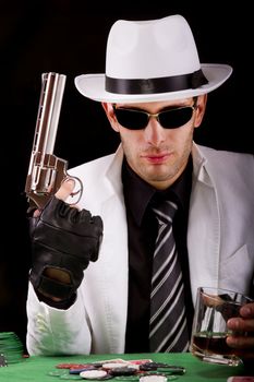 View of a gangster man playing some cards and poker, holding a gun.