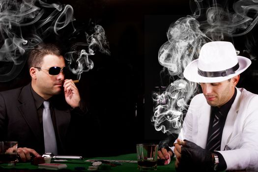 View of two gangster males playing some poker and smoking Cuban cigars.