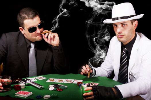 View of two gangster males playing some poker and smoking Cuban cigars.