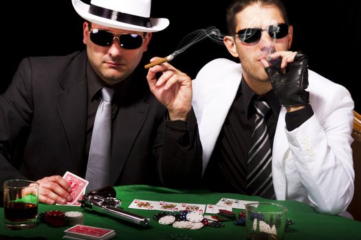 View of two gangster males playing some poker and smoking Cuban cigars.