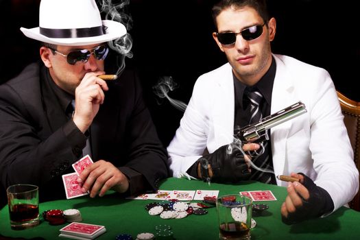 View of two gangster males playing some poker and smoking Cuban cigars.