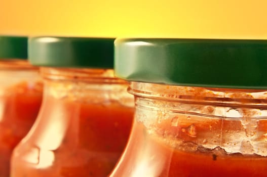 Close up on three pasta sauce jars with yellow background. Focus on foreground jar.