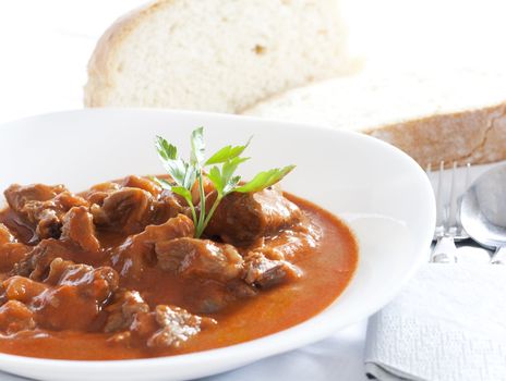 Goulash stew served in white bowl. Bread in the background