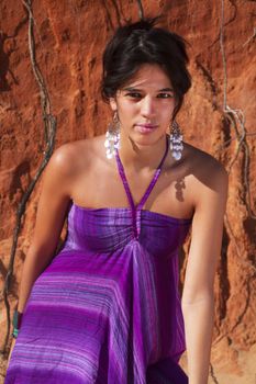 View of a beautiful young girl posing with a purple dress next to a cliff on the beach. 