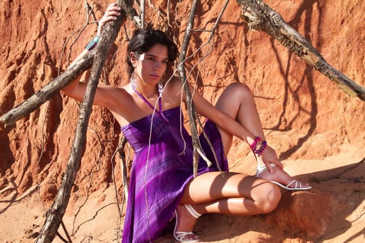 View of a beautiful young girl posing with a purple dress next to a cliff on the beach. 