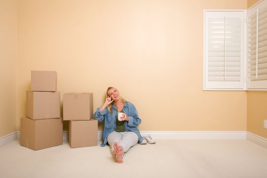 Pretty Woman Sitting on Floor with Cup Next to Moving Boxes in Empty Room.