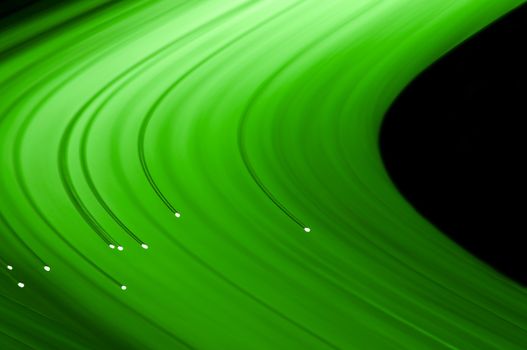 Close up capturing the ends of several illuminated green fibre optic light strands against a black background. Abstract style.