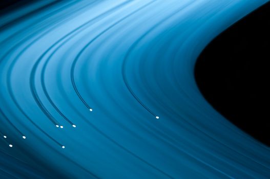 Close up capturing the ends of several illuminated fibre optic light strands against a vibrant blue background. Abstract style.
