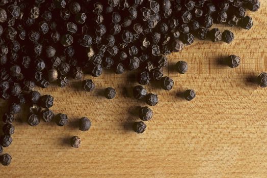 Whole black peppercorns on a wooden butcherblock surface