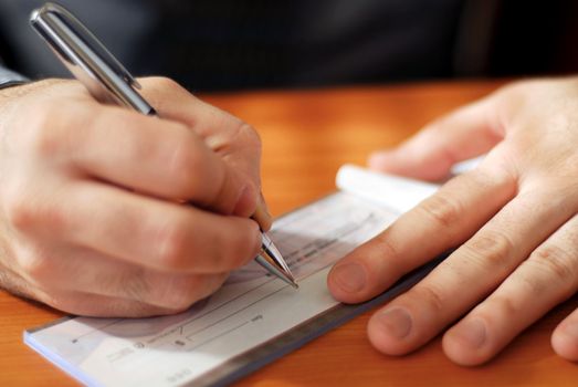 Closeup on man`s hands writing a check