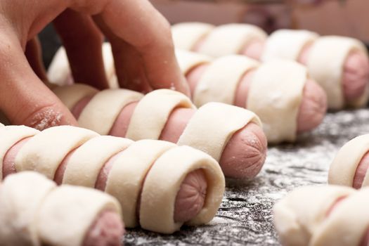 Raw sausage rolls in pastry on a baking tray