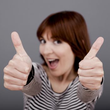 Happy young woman with thumb up over a grey background