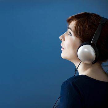 Young woman listen music with headphones over a blue wall