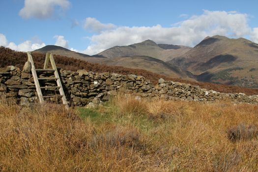 Wooden steps over a stone wall on moorland with mountains in the background.