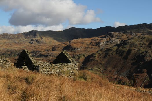 Stone walled house abandonned and derelict on grass moorland looking onto hills.