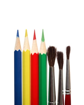 Paintbrushes and color pencils standing in a row on white background