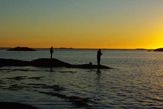 Fisherman silhouettes with angles against sunset light