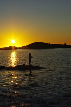 Fisherman silhouettes with angles against sunset light