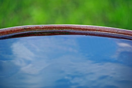 Edge of iron barrel full of water with blue sky reflection