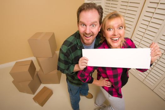 Happy Goofy Couple Holding Blank Sign in Room with Packed Boxes.