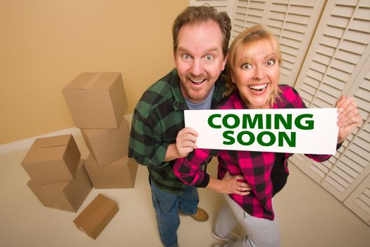 Goofy Couple Holding Coming Soon Sign in Room with Packed Cardboard Boxes.