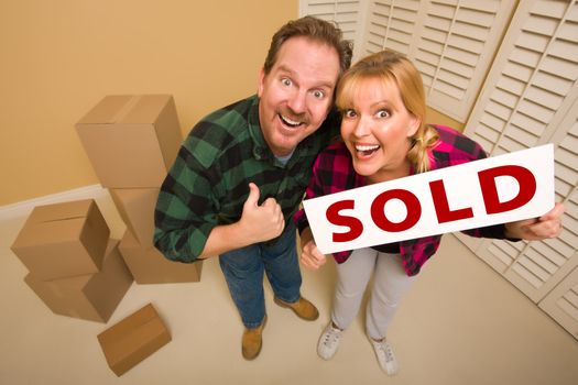 Goofy Thumbs Up Couple Holding Sold Sign in Room with Packed Cardboard Boxes.