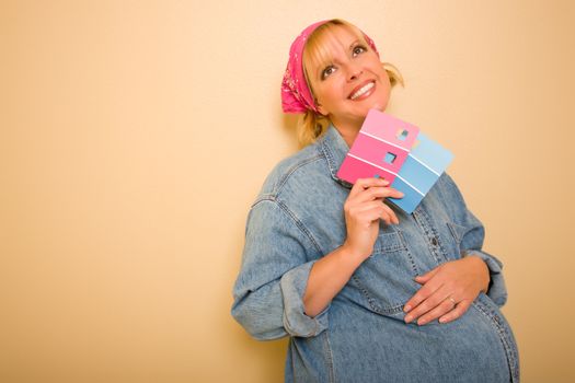 Smiling Pensive Pregnant Woman Leaning Against Wall Holding Pink and Blue Paint Swatches.
