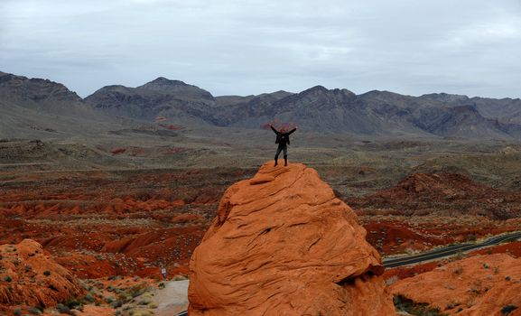 The person on a red rock. The man costs on a rock of red color against a landscape landscape.