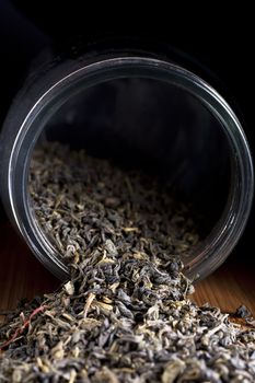 Dried Jasmine tea leaves spilling from jar with dark background.