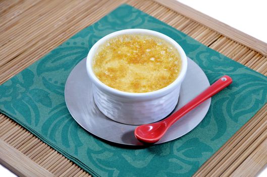 Little home-made custard with a red ceramic spoon on a green paper napkin and a bamboo tray