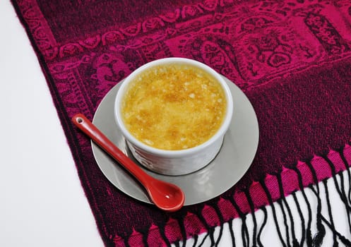 Little custard and a red ceramic spoon on an indonesian tablecloth with a white background