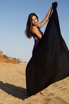 View of a beautiful young girl playful with a purple dress in the beach.