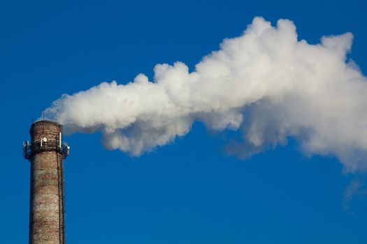 The image of a factory pipe from a smoke leaving it against the blue sky