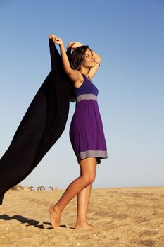 View of a beautiful young girl playful with a purple dress in the beach.