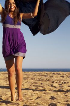 View of a beautiful young girl playful with a purple dress in the beach.