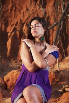 View of a beautiful young girl with a purple dress standing on a red cliff on the beach.