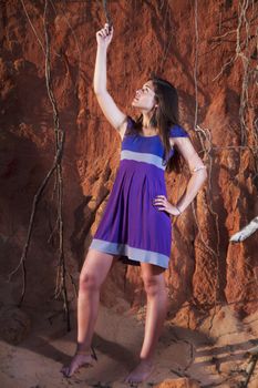 View of a beautiful young girl with a purple dress standing on a red cliff on the beach.