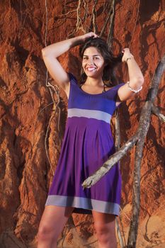 View of a beautiful young girl with a purple dress standing on a red cliff on the beach.