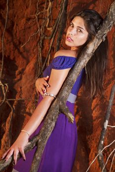 View of a beautiful young girl with a purple dress standing on a red cliff on the beach.