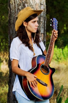 View of a beautiful young country girl with a guitar on the woods. 