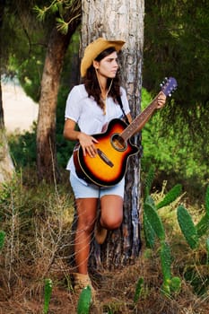 View of a beautiful young country girl with a guitar on the woods. 